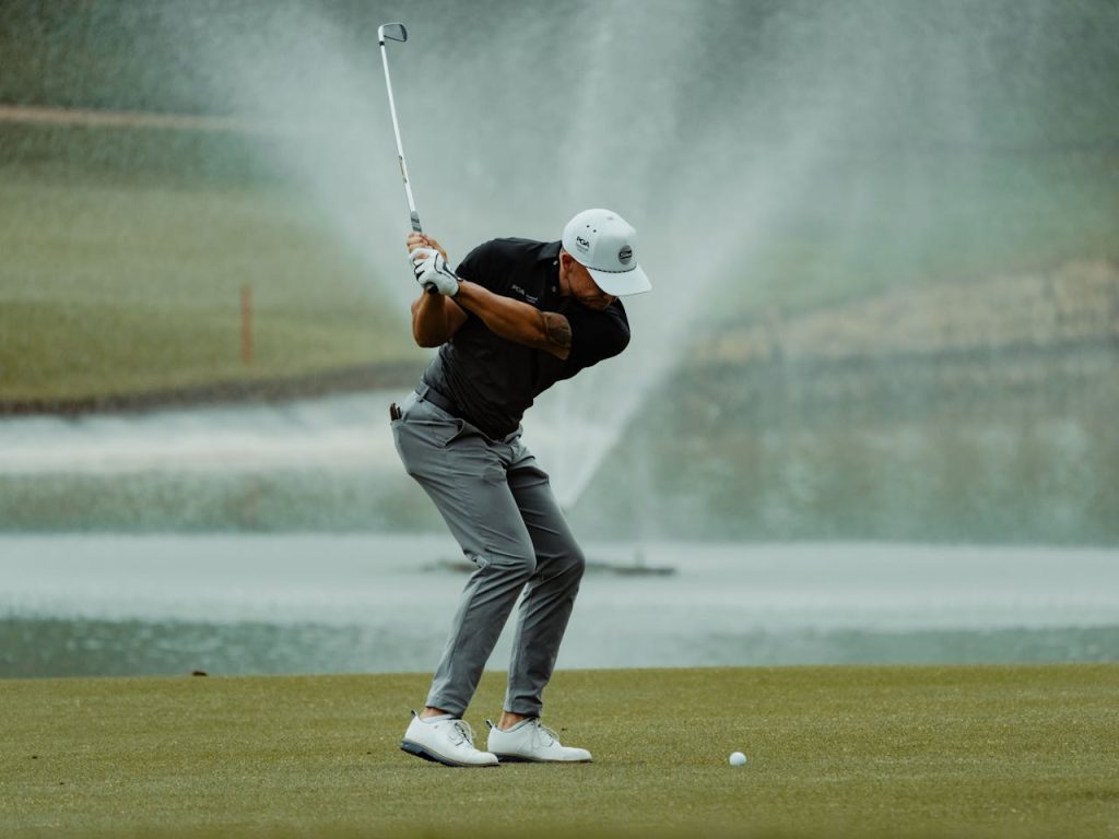 A golfer expertly swings his club on a lush green golf course with a fountain in the background.